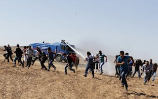 Protesters run away as an armoured army vehicle sprays water to disperse them during a pro-Kurdish demonstration near the Mursit