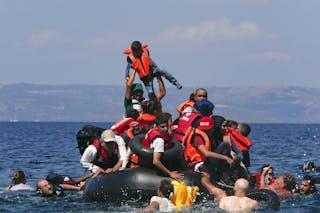 Refugee raises a child into the air as Syrian and Afghan refugees are seen on and around a dinghy that deflated some 100m away b