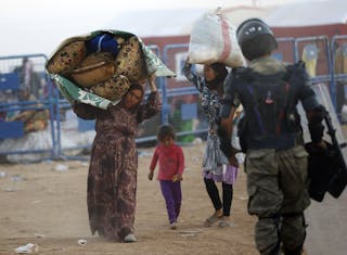 Syrian Kurdish women carry their belongings after crossing into Turkey near the southeastern town of Suruc