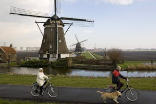 Two Dutch bicyclists pass one of four windmills of the Viermolengang, built in 1785, in Zevenhuizen