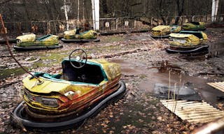 Old broken rusty metal radioactive yellow cars, children's electric cars, abandoned among vegetation, the park of culture and re