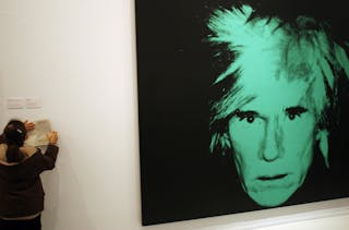 Student writes notes next to a self-portrait of US artist Andy Warhol in Madrid