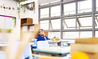 asian pupil sitting alone in classroom looking up at the ceilings.