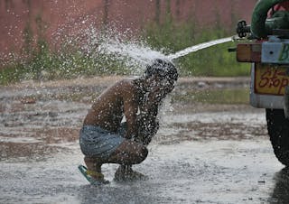 A man bathes while sitting under a water tanker on a hot summer day on the outskirts of Jammu