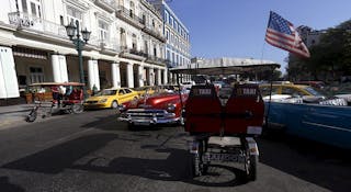 A tricycle taxi with a U.S. flag is parked on a street in Havana