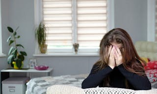 Photo of brunette girl with long dark hair in the room. She is very upset and sad. Sits on the sofa in front of the camera and i