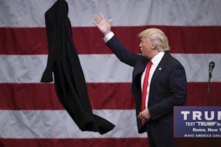 U.S. Republican presidential candidate Donald Trump tosses off his overcoat as he speaks at a campaign event in an airplane hang