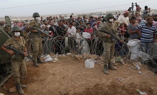 Turkish soldiers stand guard as Syrian Kurdish refugees wait behind the border fences to cross into Turkey near Suruc in Sanliur