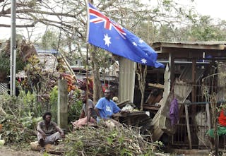 Local residents sit outside their damaged homes surrounded by debris on a street after Cyclone Pam hit Port Vila, the capital ci