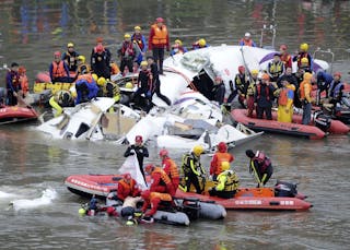 Emergency personnel retrieve the body of a passenger from the wreckage of a TransAsia Airways aircraft after it was crashed in a