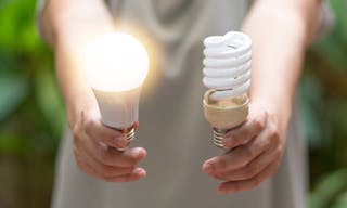 Power saving concept. Hands holding new Light Emitting Diode ( LED ) light bulb with light on and blur spiral compact-fluorescen