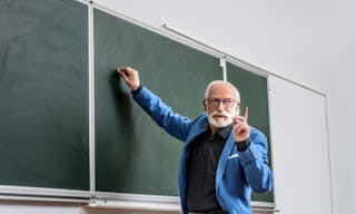 Senior lecturer writing something on blackboard and showing one finger up — Photo by IgorVetushko