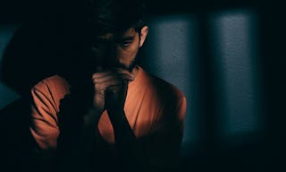 Prisoner man in dark cell depressed or praying