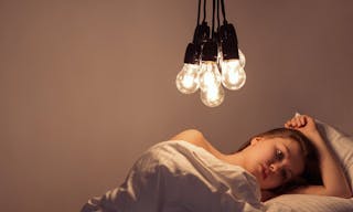 A girl lies in bed under big light bulbs can't fall asleep. Concept picture. Insomnia. Psychology.