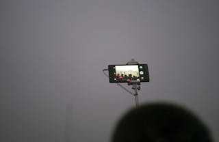 Tourist uses his mobile phone to take picture during a flag-raising ceremony amid heavy smog at the Tiananmen Square, after the 