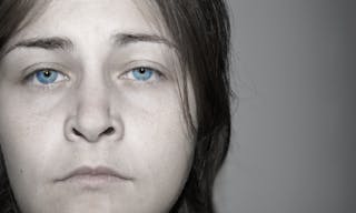 Dramatic faded portrait of a depressed, sad, young woman with stunning eyes. Almost black and white with real color eyes.