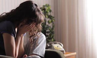 Depressed young woman sitting in chair at home