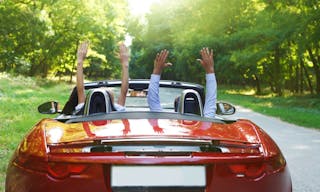 Happy free couple driving in red retro car cheering joyful with arms raised. Road trip travel concept