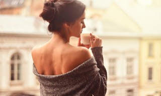 Beautiful woman holding cup of coffee standing on the balcony. Fascinated by the aroma of coffee - 圖片