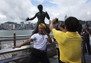 A tourist poses in front of a bronze statue of the late kung fu legend Bruce Lee on the waterfront of Hong Kong