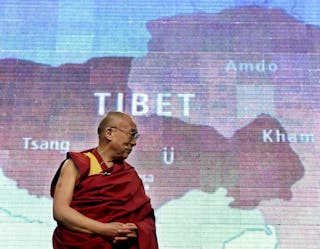 Dalai Lama stands beneath map of Tibet projected on screen during public talk in Washington