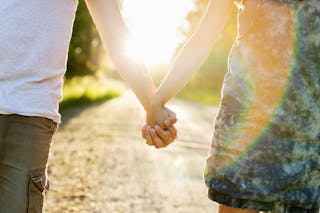 Midsection of couple holding hands on dirt road against bright sun