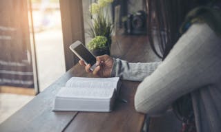 Study and technology concept.Sad woman (christian) hand on bible at coffee shop,send message by mobile phone.People side view,ho