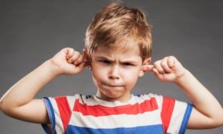 Young boy covering ears against gray background