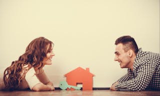 real estate, family and couple concept - smiling couple lying on floor with symbol house and key daydreaming at home, vintage fi