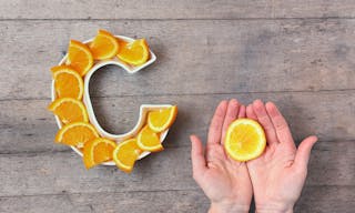 Vitamin C nutrient in food concept. Plate in shape of letter C with orange slices and woman hand with citrus on wooden backgroun