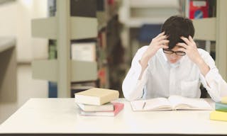 Young student study hard in library. Asian male university student doing study research in library with books and on desk and sm