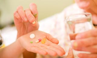 A young doctor giving medications - drugs and vitamins - and a glass of fresh water to an elderly woman.