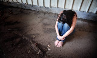 A sad woman is sitting alone on the cold concrete behind a shed