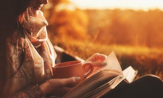 Beautiful girl in autumn forest reading a book covered with a warm blanket.a woman sits near a tree in an autumn forest and hold