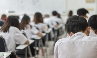 Blur school or university students writing answer doing exam in classroom, view from back of the class for education background