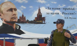 A Russian policeman stands next to a wall bearing an image of Russia's President Vladimir Putin