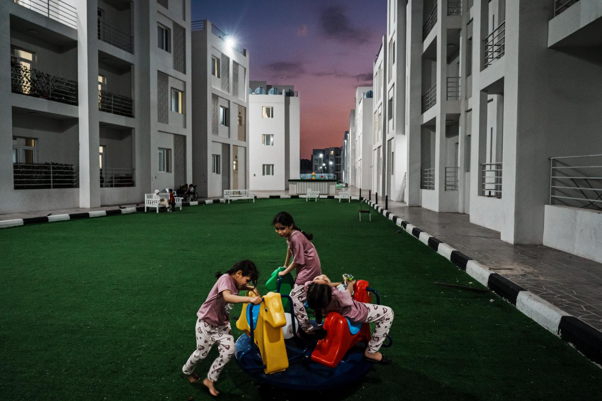 Three children play in the evening on a long stretch of artificial turf between apartment buildings