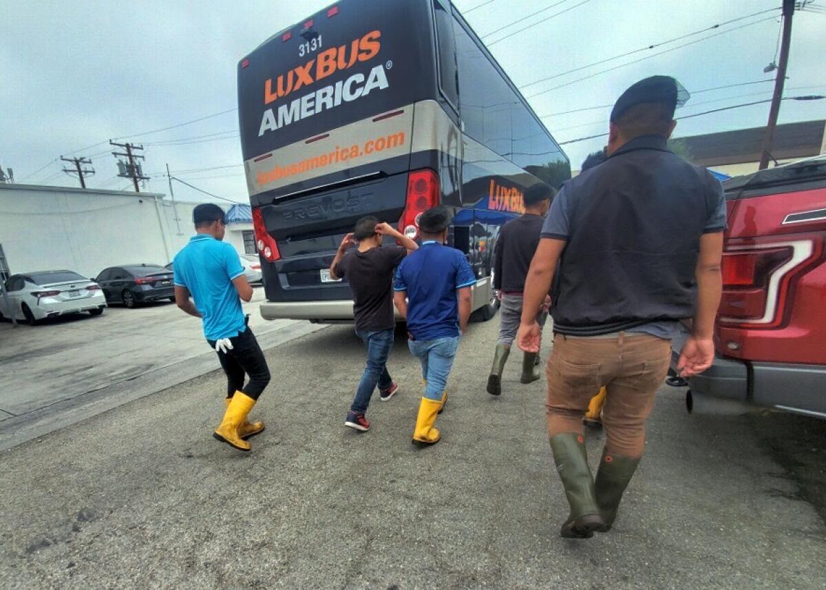 Workers in rubber boots walk through a parking lot near a charter bus.