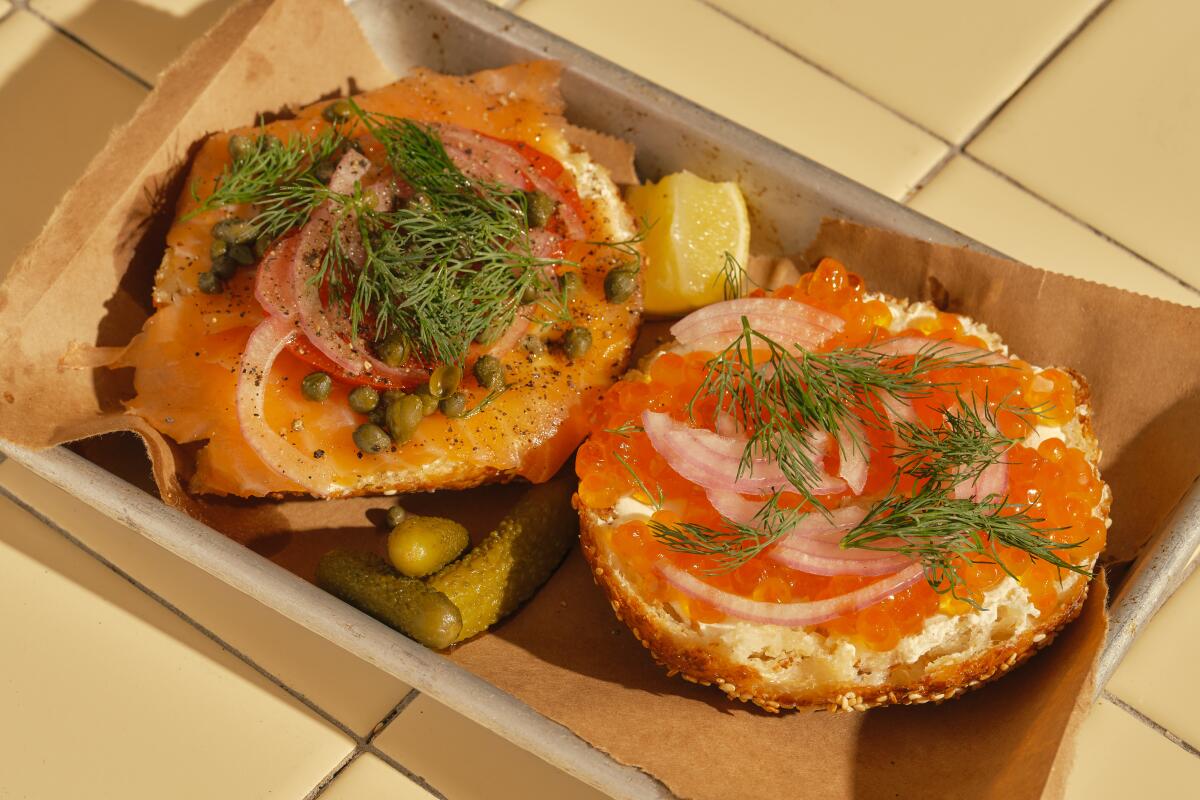 Two halves of a bagel, topped with smoked salmon, dill and roe, in a cardboard dish