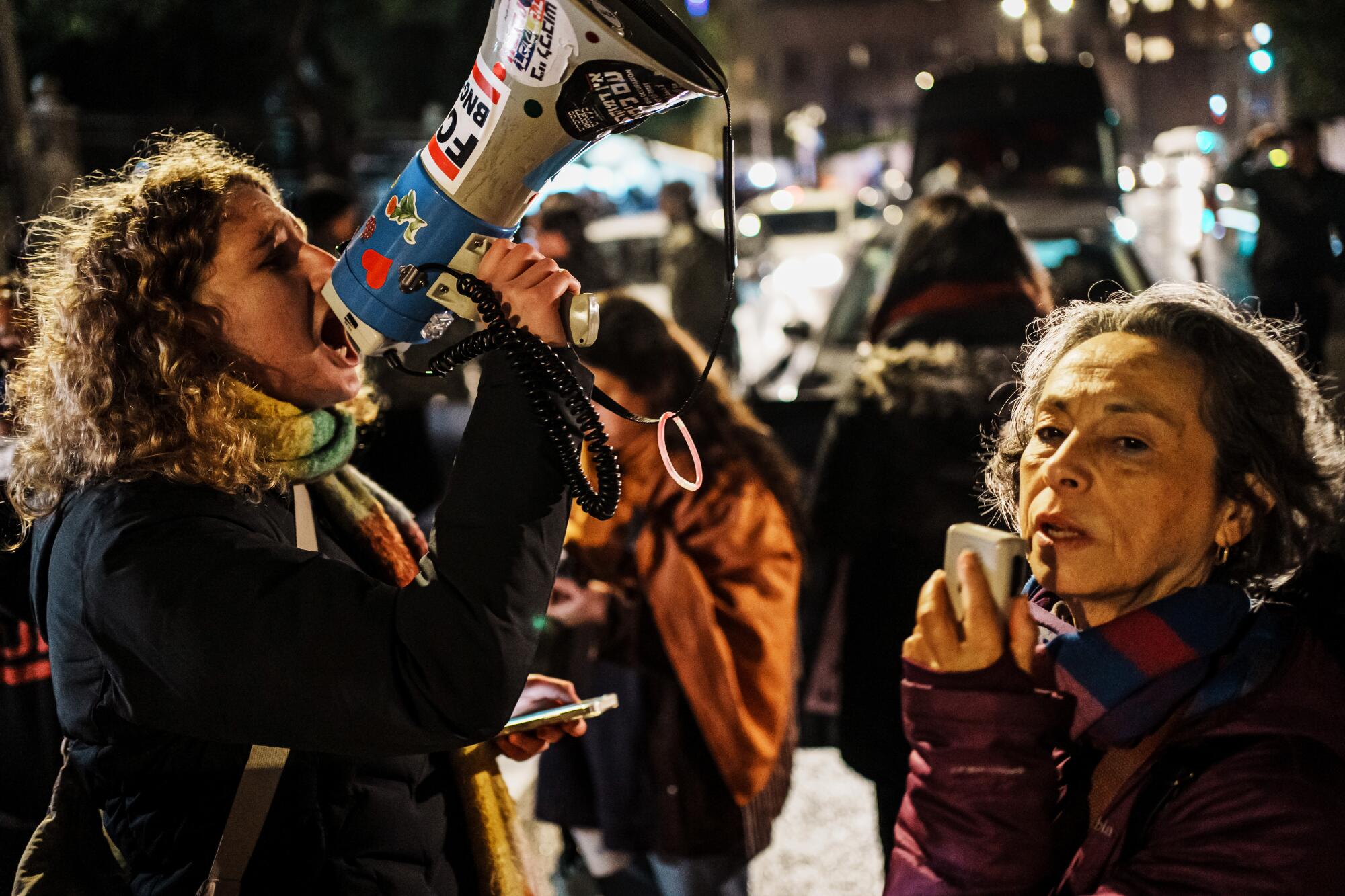 A woman speaks into a raised bullhorn in a crowd.