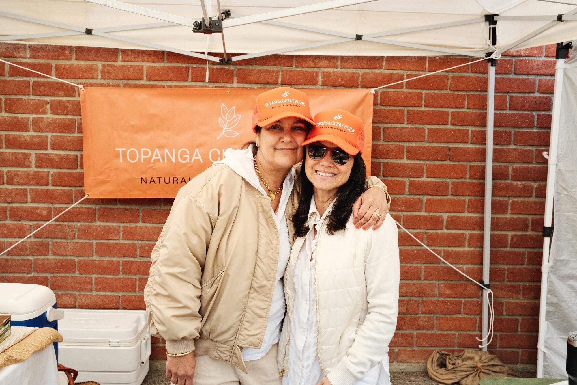 Claudia Joshi, left, with an arm around Destiny London at their orange-tented Topanga Curry House stall