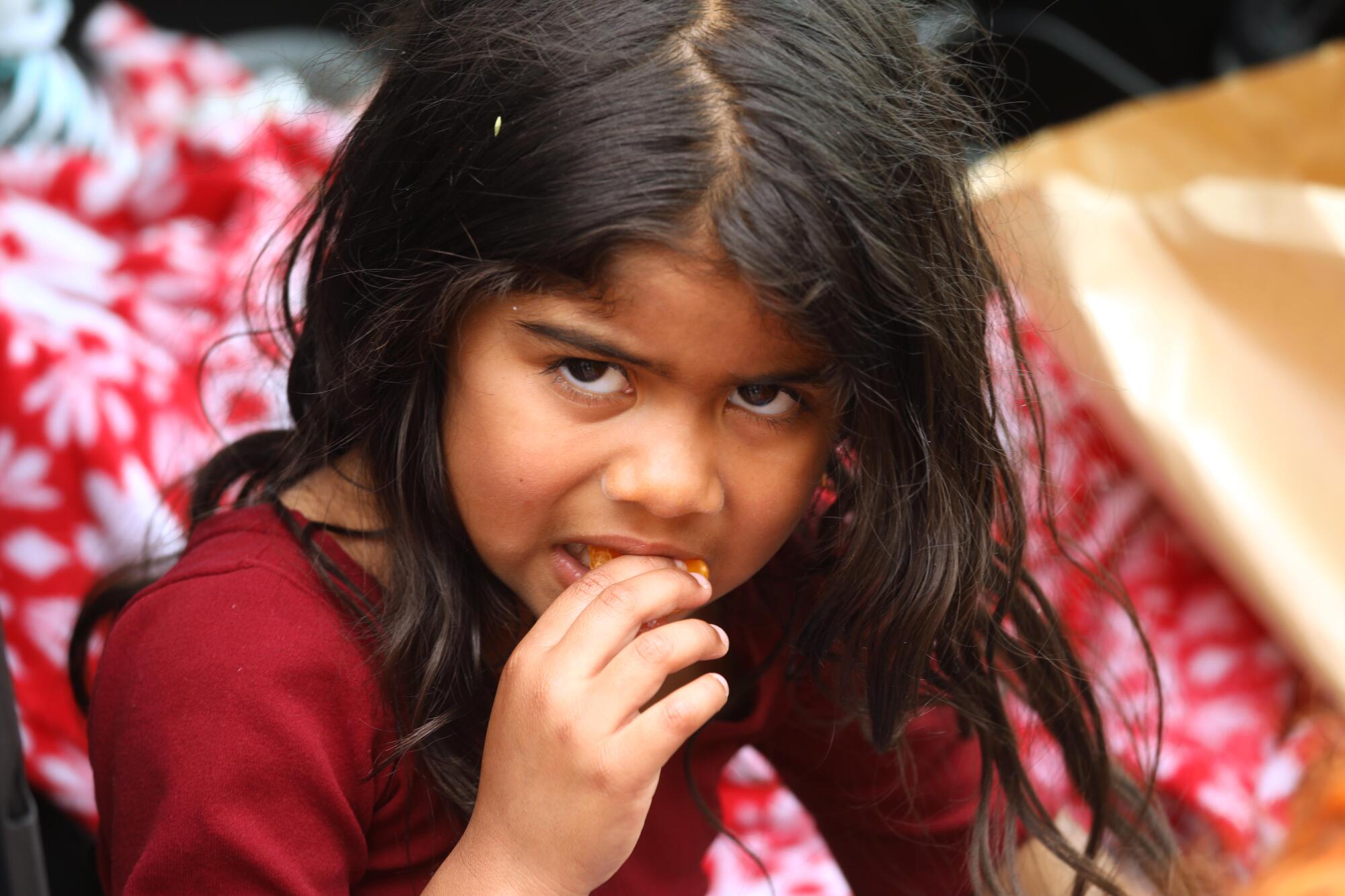 Migrant child Celeste, 5, eats a tangerine inside the car where she has been living 