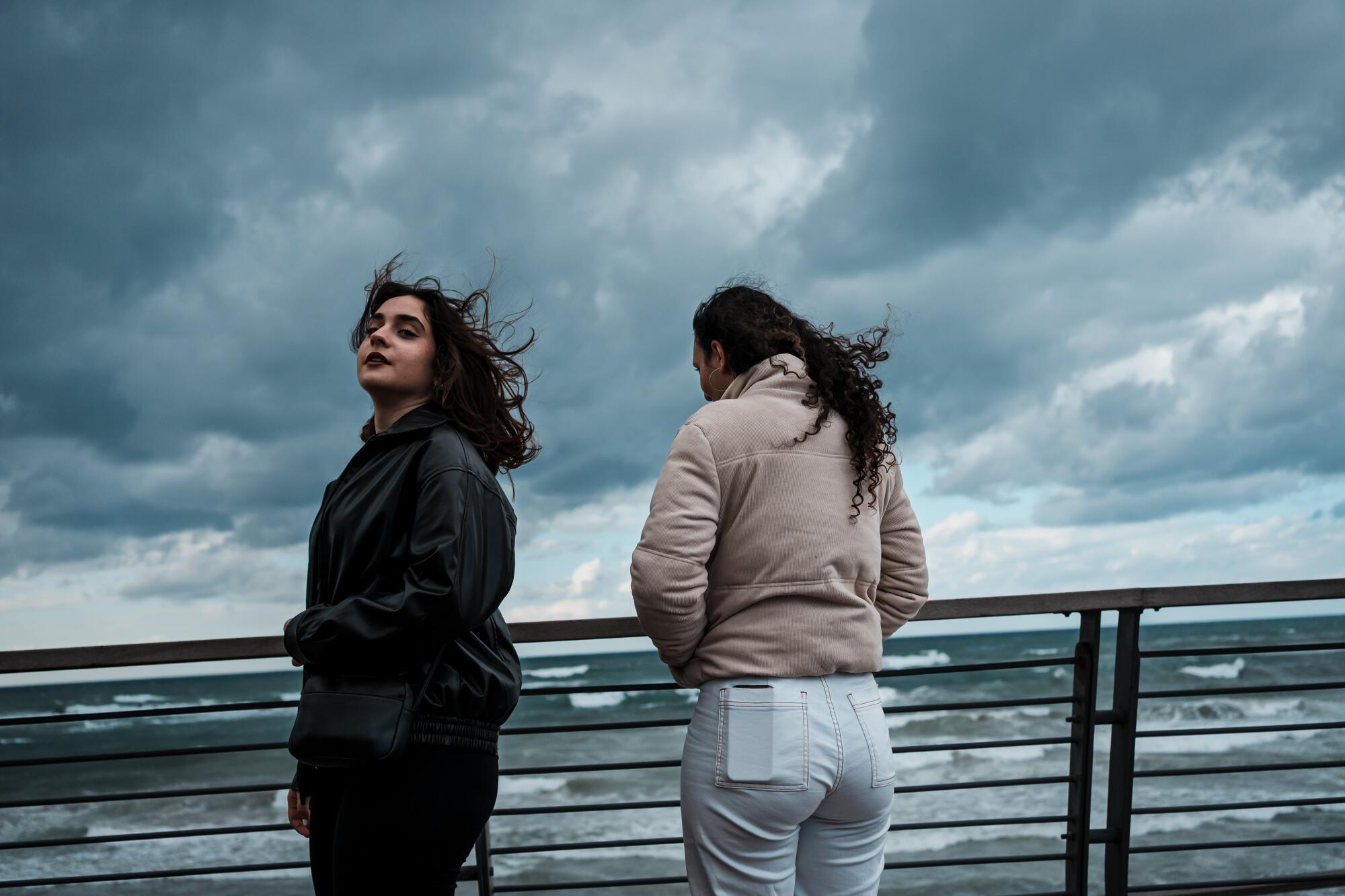 Two teenage girls wearing winter jackets at a stormy beach 