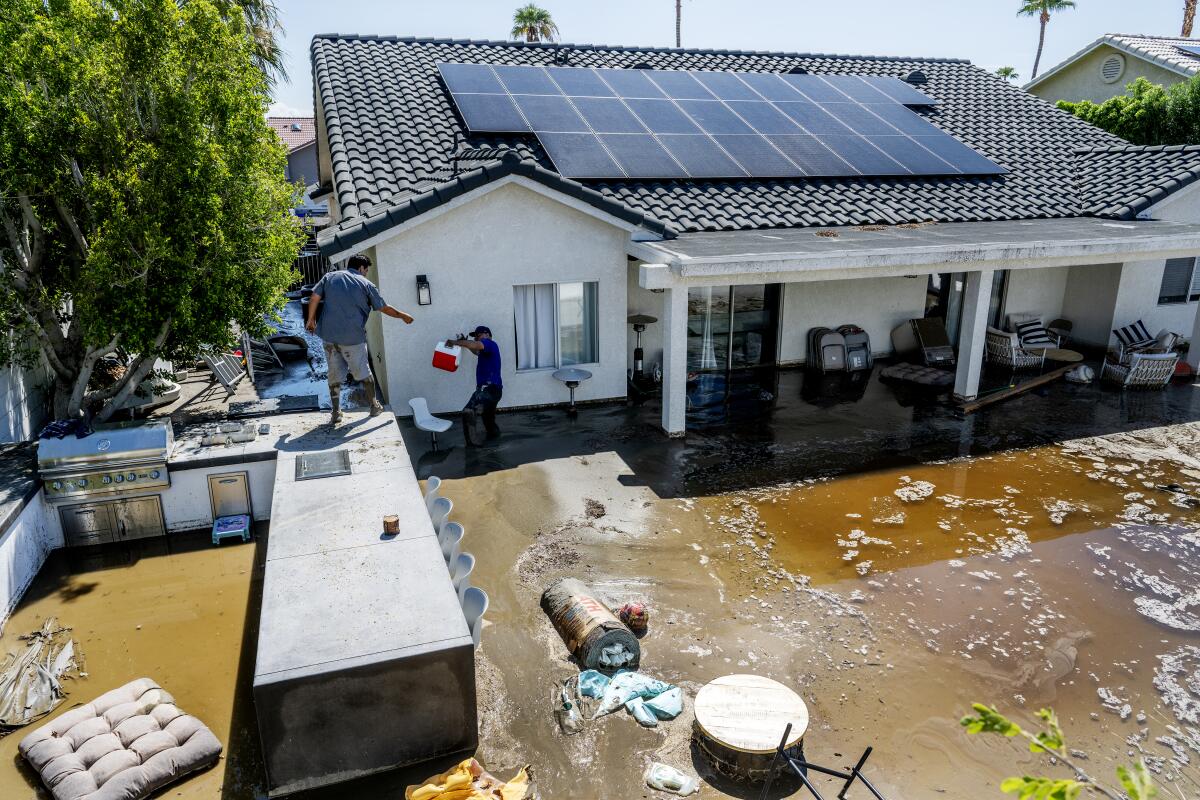 Two man standing on furniture outside as the backyard is flooded. 