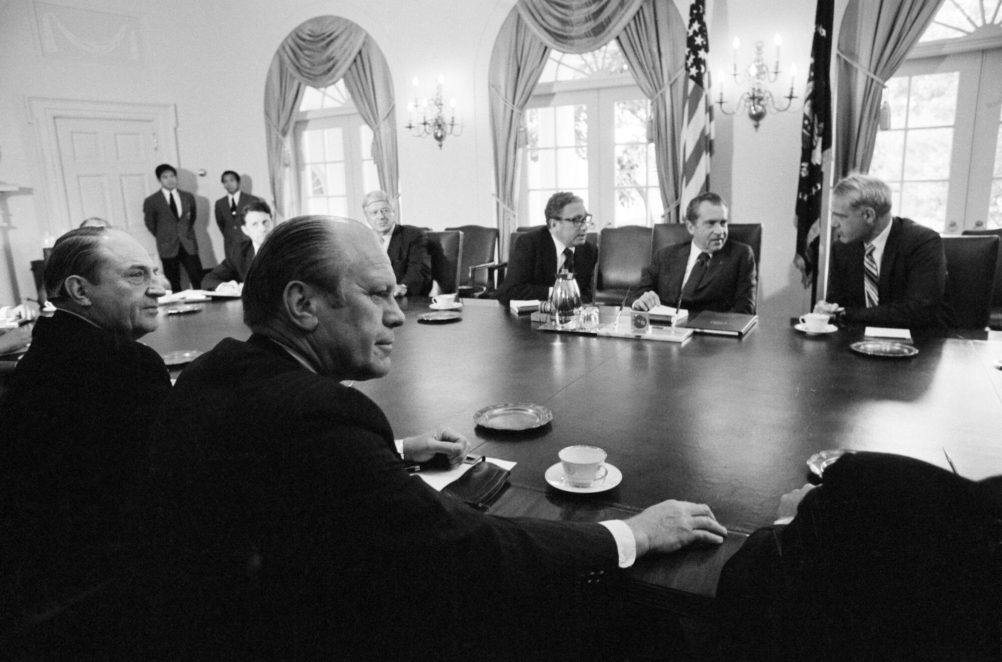 A black-and-white photo of officials at a table in an ornate room, Gerald Ford in the foreground across from Richard Nixon
