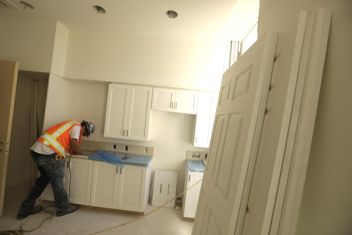 A construction worker sands a kitchen counter.