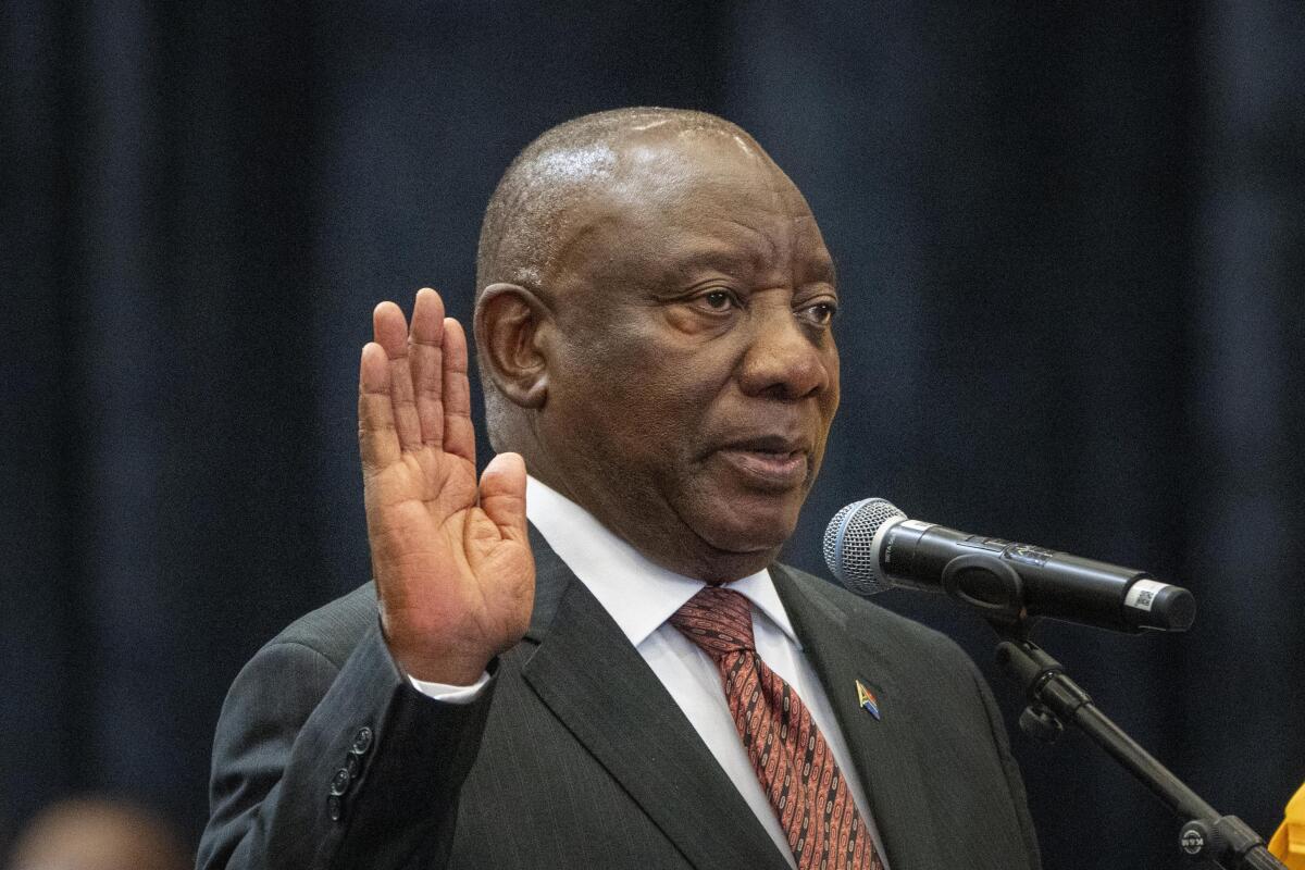 South African President Cyril Ramaphosa raises his hand and speaks into a microphone.