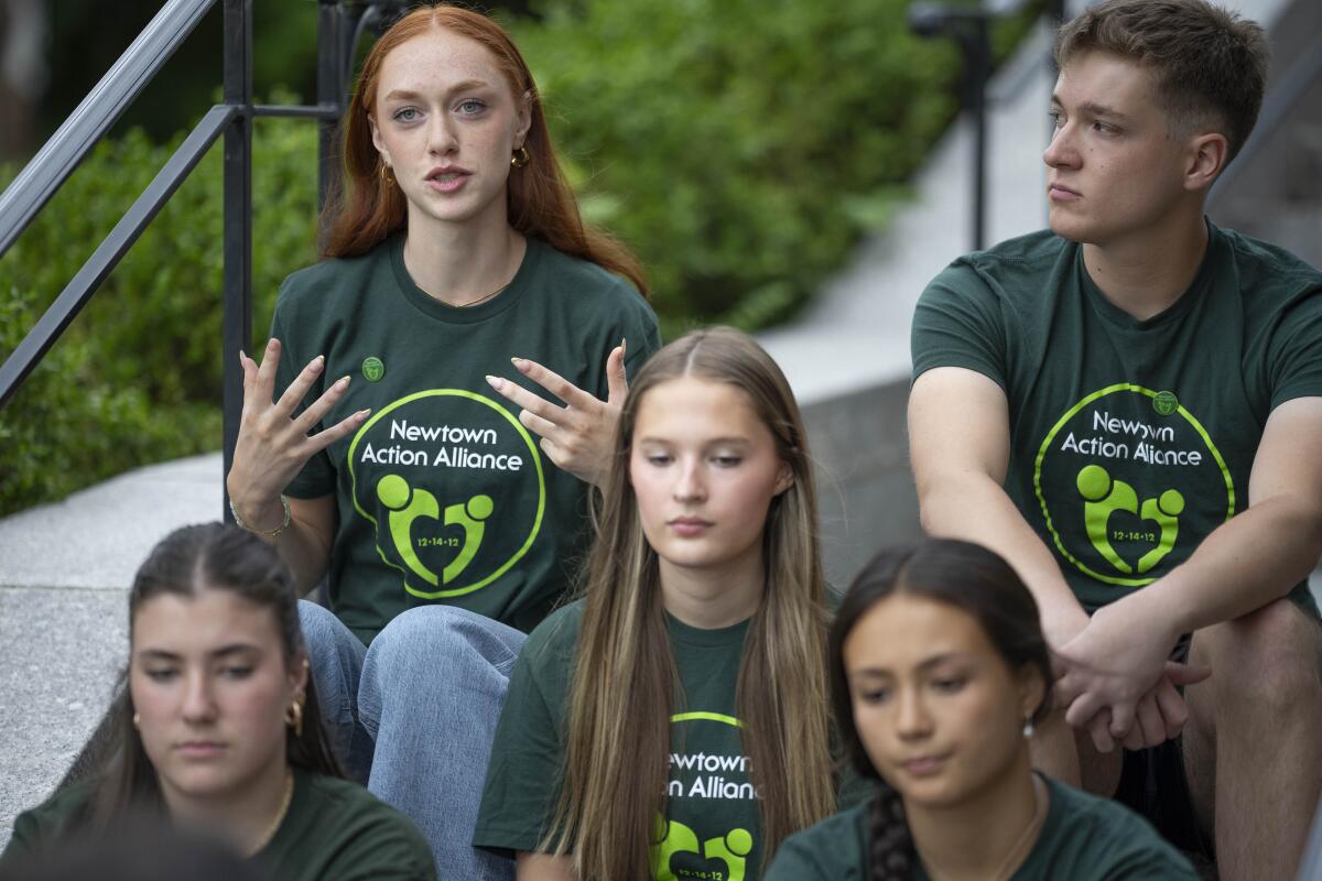 High school students wearing green "Newown Action Alliance" sit on concrete steps. 