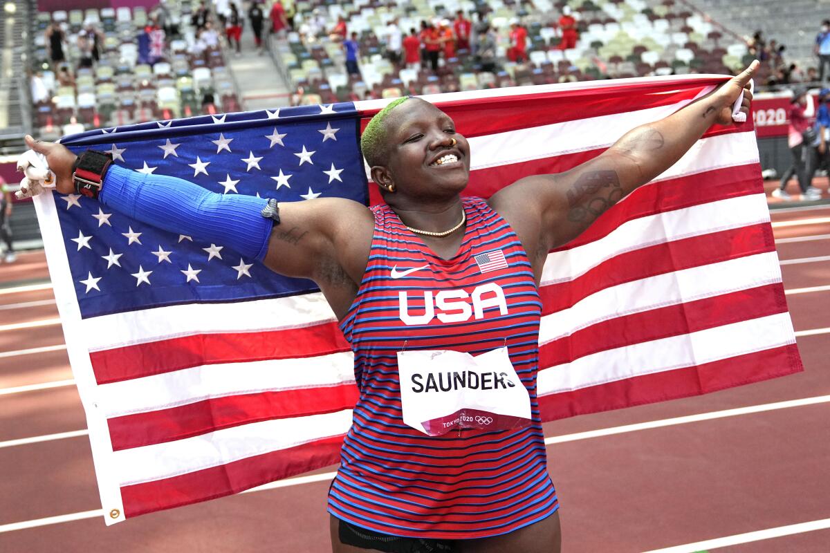 U.S. shot putter Raven Saunders smiles and carries a U.S. flag behind her.