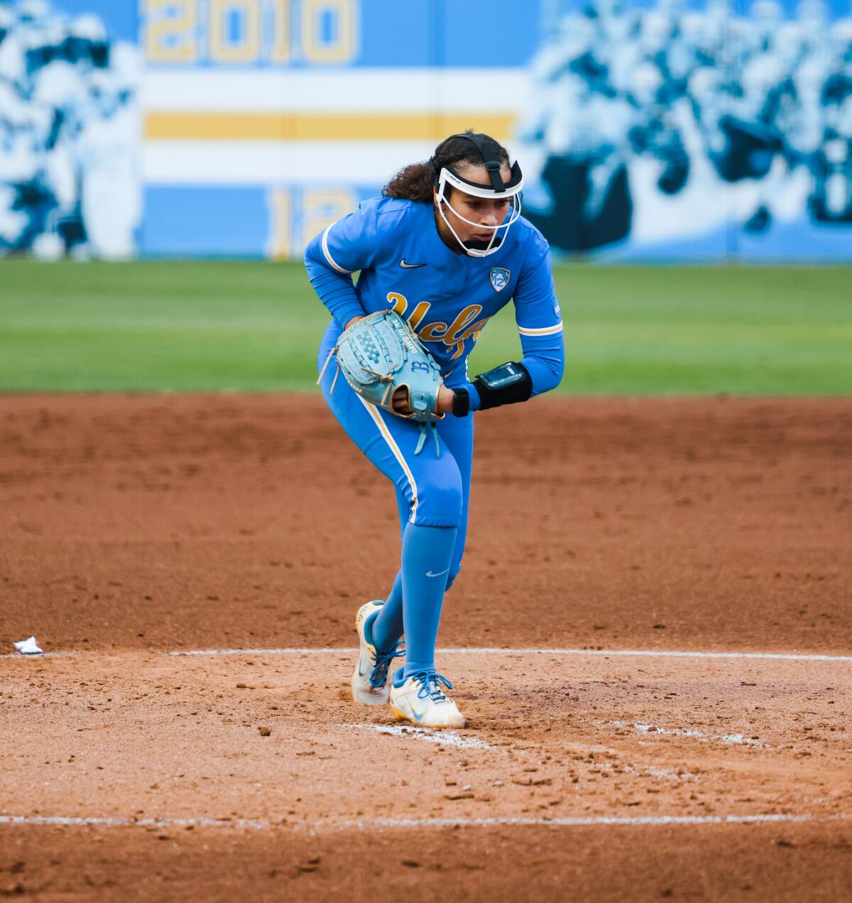 UCLA right-hander Taylor Tinsley winds up in the pitching circle with a face mask and blue uniform